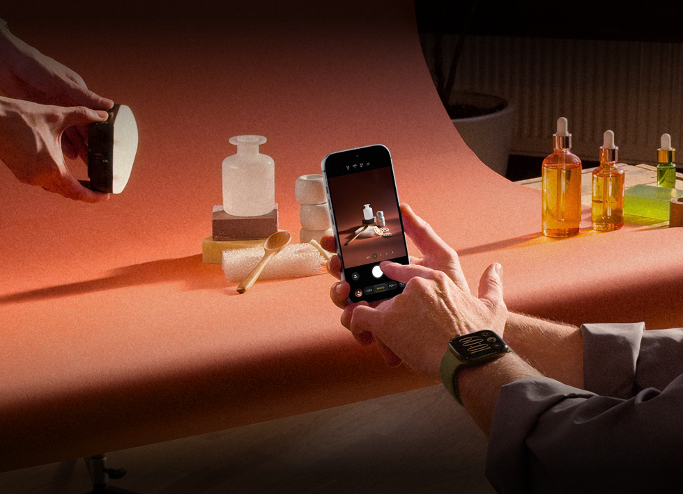 Séance photo dans un environnement professionnel, une personne utilise un iPhone pour photographier des produits sur un fond, une autre personne tient une lampe