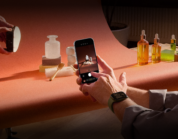 Séance photo dans un environnement professionnel, une personne utilise un iPhone pour photographier des produits sur un fond, une autre personne tient une lampe