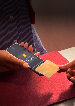 Une main approche une carte bancaire d’un iPhone pour finaliser une transaction